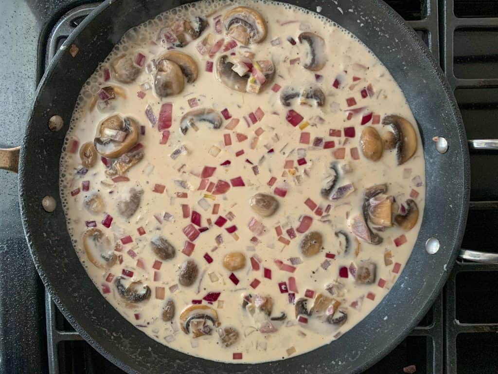 mushrooms and onions in a creamy sauce in a saute pan