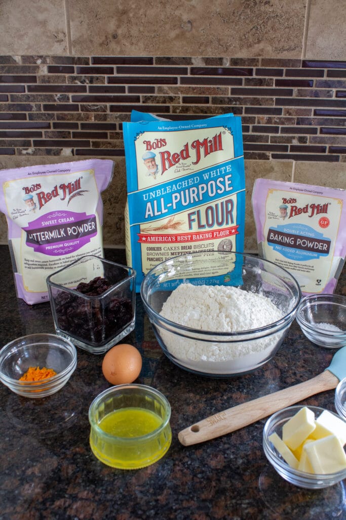 Bob's Red Mill flour, baking powder, and buttermilk powder on a counter with ingredients for cherry scones