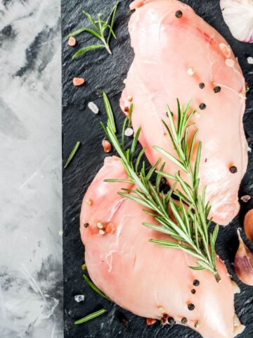 two chicken breasts on a gray slate with rosemary on top